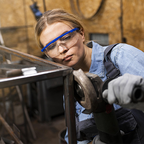 Une femme en contrat CDD qui travaille dans le bâtiment avec des lunettes et des gants de sécurité.